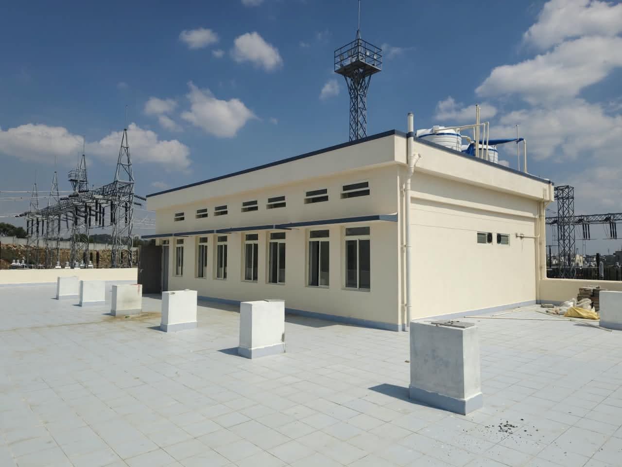 A single-storey building at the edge of the switchyard, a lighting mast beyond