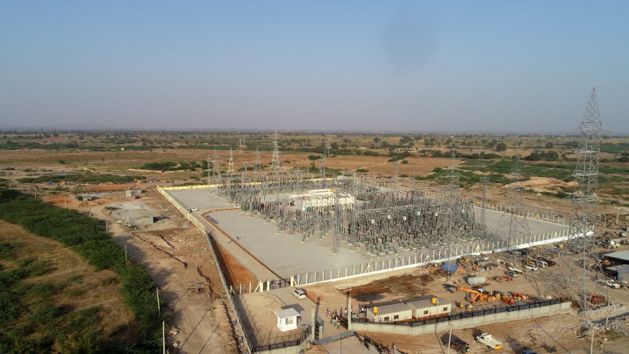 A sub-station switchyard from the air, a transmission tower beyond
