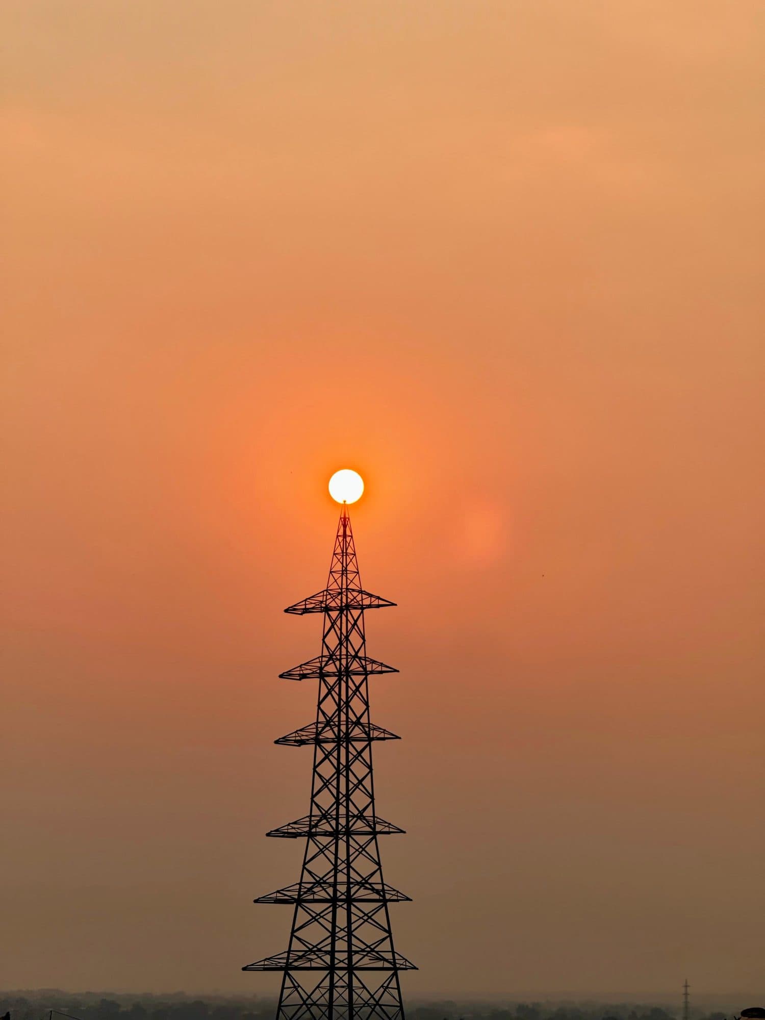 The sun resting on the top of a transmission tower